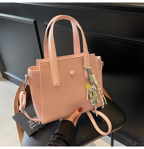 Sac seau rose avec texture tressée, cuir mat et breloque chiot posé sur une chaise noire