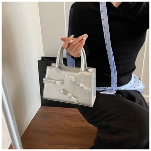 Detailed view of silver metallic handbag featuring 3D bow accents and smooth top handle