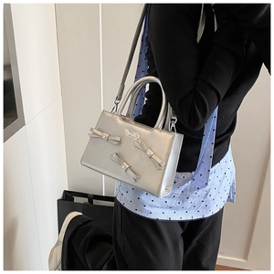 Detail of silver crossbody bag featuring decorative bows and metallic texture finish