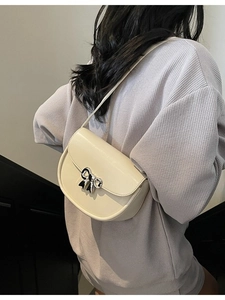 Creamy saddle bag with metallic bow buckle shown on model in a modern staircase setting