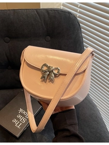 Pink patent leather saddle bag with silver metal bow clasp held in front of a dark sofa