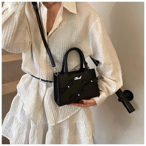 Detail of black bow handbag with pearl accents and detachable shoulder strap on steps
