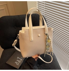 Détail du sac seau tissé crème avec breloque ours et bandoulière sur une chaise