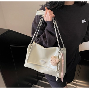 Detail view of the beige patent leather tote bag with elegant chain strap and plush charm