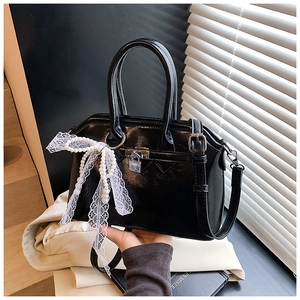 Detail of glossy black leather handbag featuring white lace pearl bow and gold metal clasp