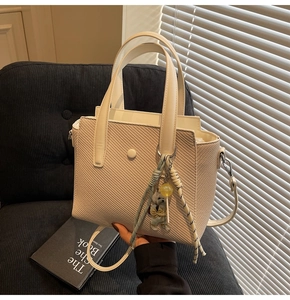 Détail du sac seau tressé crème avec breloque ours en peluche et ombre douce intérieure
