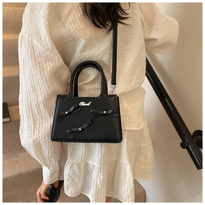 Detail of black leather bow bag with pearls and silver metallic logo on woman's outfit