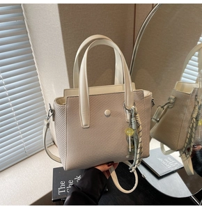 Détail du sac seau tissé beige avec poignées en cuir et breloque en corde rayée