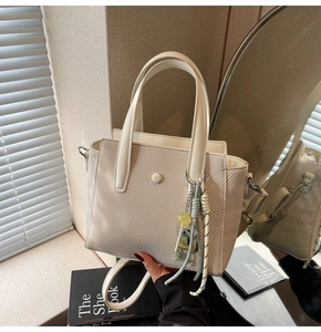 Détail du sac seau beige avec poignées et pendentif en peluche sous une lumière naturelle