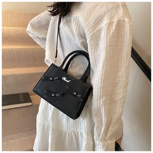Detail of black crossbody bag with three pearl-studded bows and a metallic logo