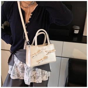 Detail of cream crossbody bag featuring decorative bows and metallic logo on textured PU leather