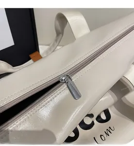 Close-up of smooth silver metal zipper on cream leather travel tote bag with lettering