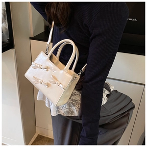 Detail of cream crossbody bag with bow accents and silver metal hardware straps