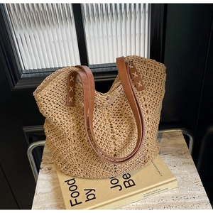 Detail of woven straw tote bag with brown leather handles and decorative cross stitching
