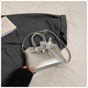 Detail of silver metallic square bag featuring white lace trim and pearl charms