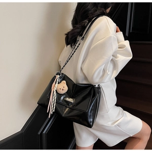 Detail of black leather shoulder bag with metal chain strap and cute bear charm pendant