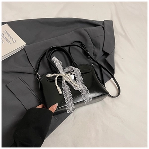 Detail of black glossy handbag featuring white lace bow and pearl pendant decoration