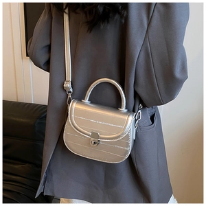 Close-up of metallic silver saddle bag with adjustable shoulder strap and turn-lock