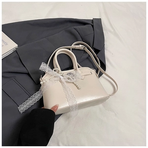 Detail of a creamy white handbag featuring lace bows and pearl charms on fabric