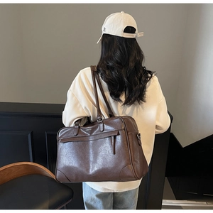 Détail du grand sac de voyage en cuir marron avec poche zippée porté par le mannequin