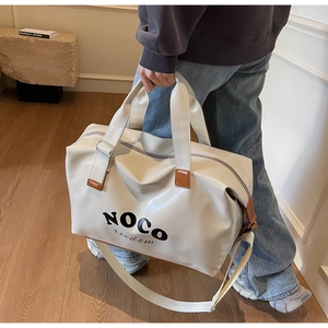 Detail of a large cream PU leather travel bag with brown handles and shoulder strap