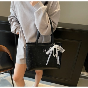 Detail of black embossed tote bag with elegant white lace bow and pearl chain charm
