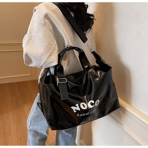 Detail of glossy black large tote bag with NOCO freedom text and wide nylon shoulder strap