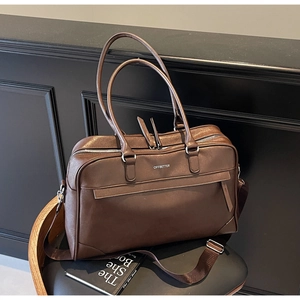 Détail d'un grand sac de voyage en cuir marron foncé avec bandoulière et deux poignées