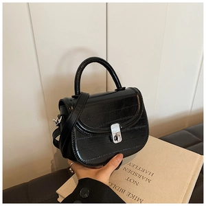 Detailed view of black embossed leather saddle bag with silver metal twist-lock and strap