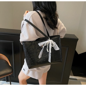Detail of black embossed tote bag with lace bow and pearl charm on a shoulder strap