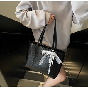 Detail of black embossed tote bag with white lace bow and pearl charm ornament