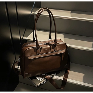 Détail du sac de voyage marron en similicuir avec bandoulière sur escalier gris
