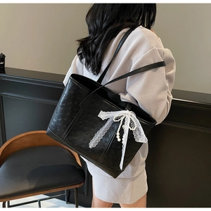 Detail of black tote bag with embossed smileys, white lace bow, and pearl tassels
