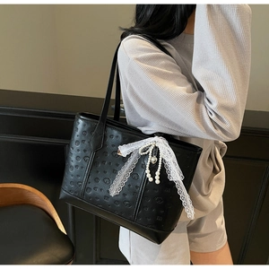 Detail of black PU leather tote bag with bear embossing and lace bow accessory