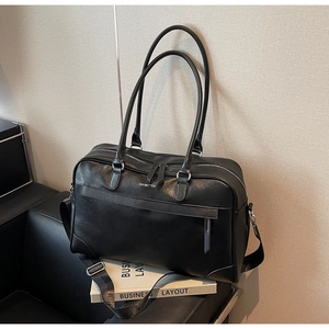 Détail du sac de voyage en similicuir noir avec bandoulière et logo imprimé