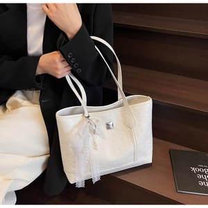 White leather tote bag with embossed pattern and pearl tassel accessory on a model