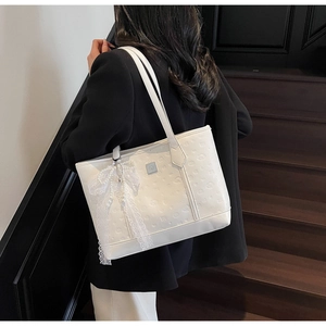 Detail of white embossed tote bag featuring a lace bow and pearl charm on the shoulder strap