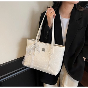 Detail of white embossed tote bag featuring lace bow and pearl pendant accessories