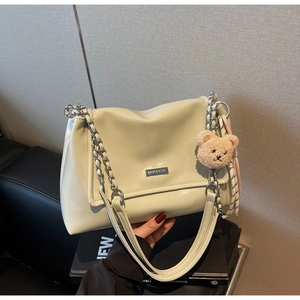 Close-up of cream shoulder bag with silver chain strap and a plush bear pendant charm