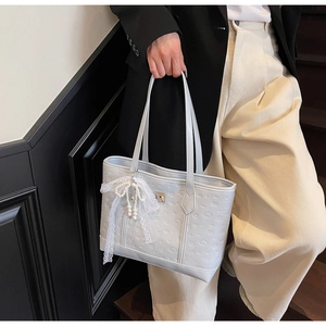 Detail of grey embossed tote bag featuring a white lace bow and elegant pearl charm