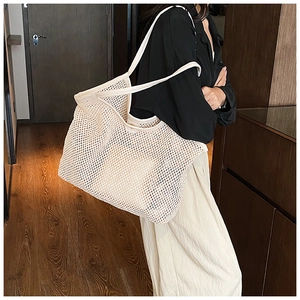 Detail of a beige woven mesh tote bag with smooth handles carried by a model