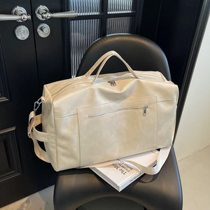 Dettaglio della grande borsa tote beige con tracolla su una poltrona in pelle nera