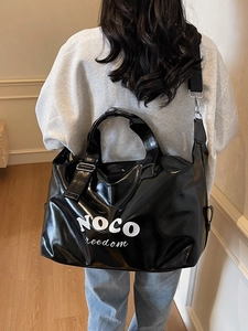 Black high-shine travel tote with white NOCO lettering shown on a model for scale