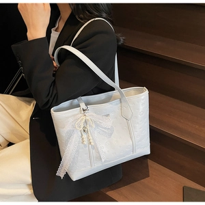 Close-up of light blue embossed tote bag with lace pearl bow charm and floral texture