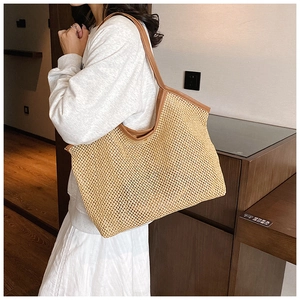 Straw tote bag with brown leather straps shown on a model in a cozy indoor setting