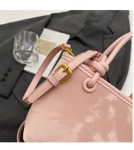 Detail of light pink patent leather shoulder bag with adjustable strap and gold buckle