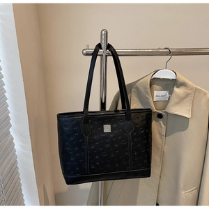 Detail of black embossed leather tote bag with silver logo plaque on beige coat background