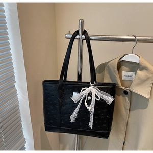 Detail of black tote bag featuring embossed heart patterns and lace bow with pearl charm