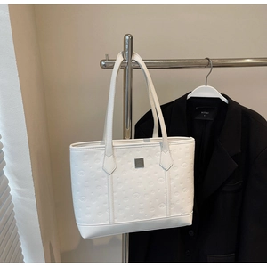 Close-up of white embossed tote bag with silver metal plaque on a studio hanger