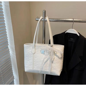 Close-up of a white leather tote bag featuring 3D embossed texture and pearl lace bow